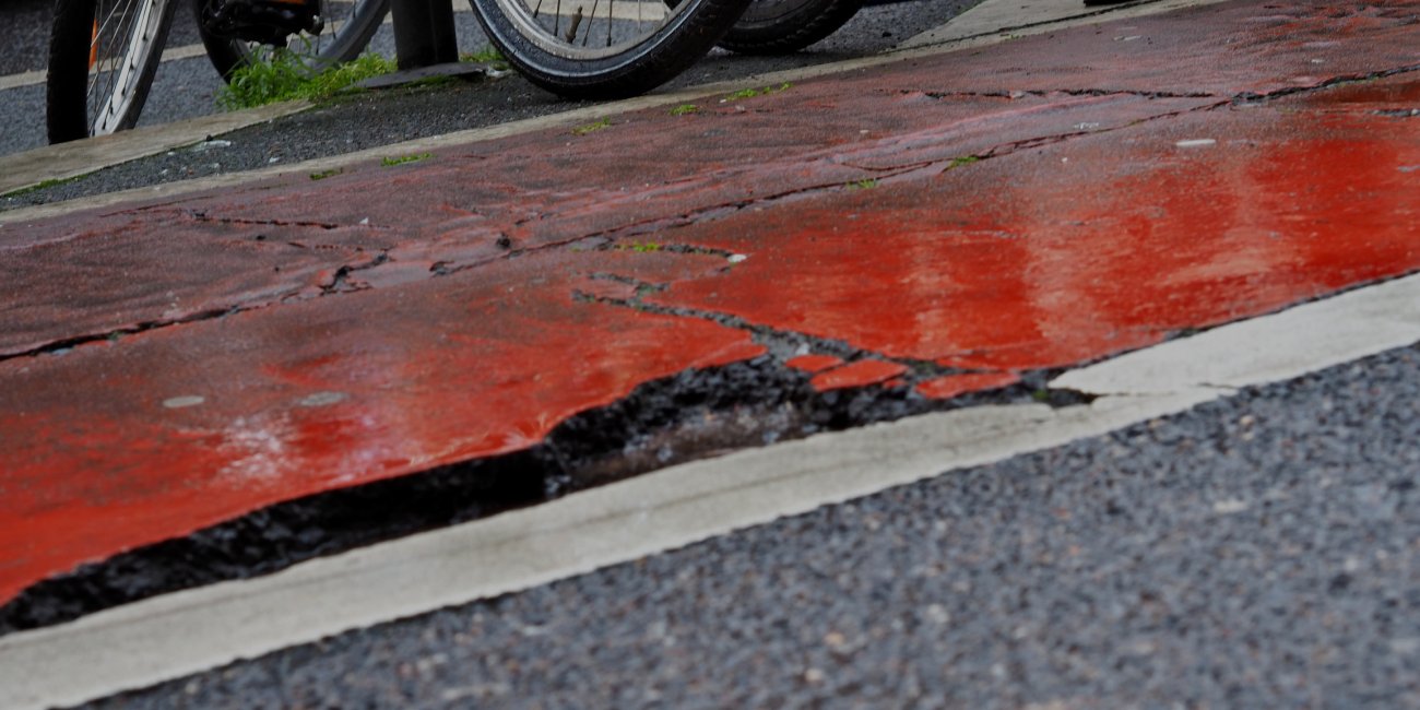 Rot markierter Fahrradweg mit tiefem Loch im Asphalt