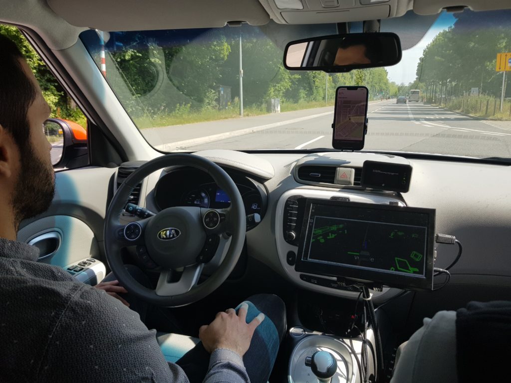 Cockpit-Ansicht eines autonom fahrenden Testfahrzeugs mit Bildschirm am Armaturenbrett und Sicherheitsfahrer ohne Hände am Lenkrad