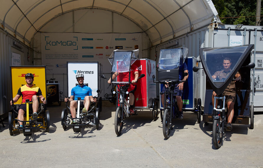 Foto: Fünf Lastentrasnportfahrräder stehen nebeneinander, in denen jeweils ein Fahrer sitzt