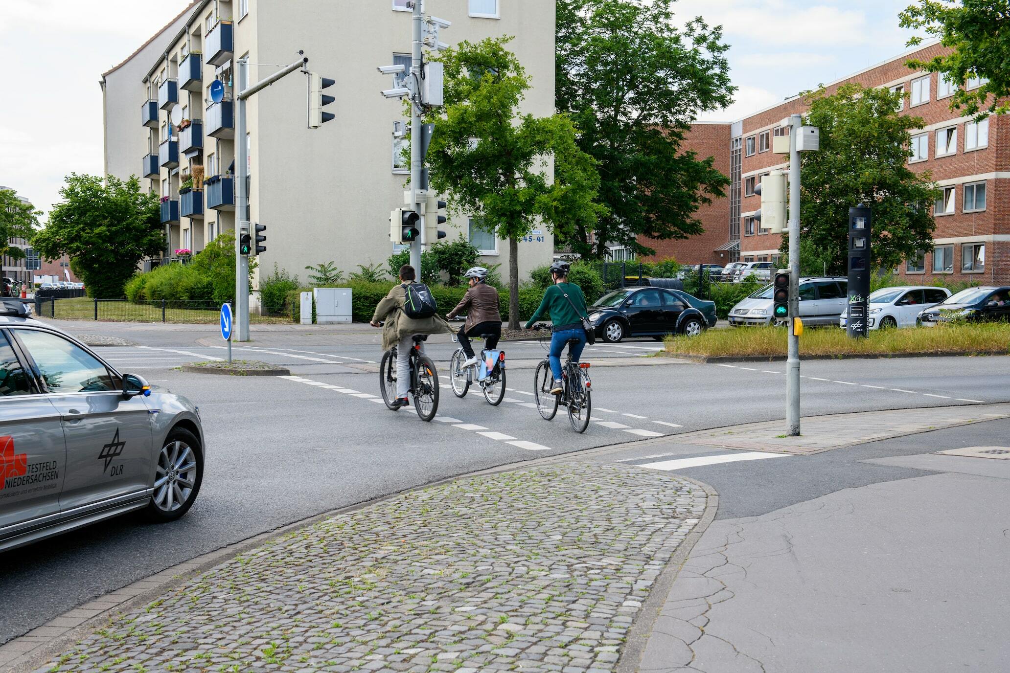 Ein Auto mit Aufklebern des DLR und des digitalen Testfelds Niedersachsen gewährt beim Rechtsabbiegen drei Fahrradfahrer*innen die Vorfahrt