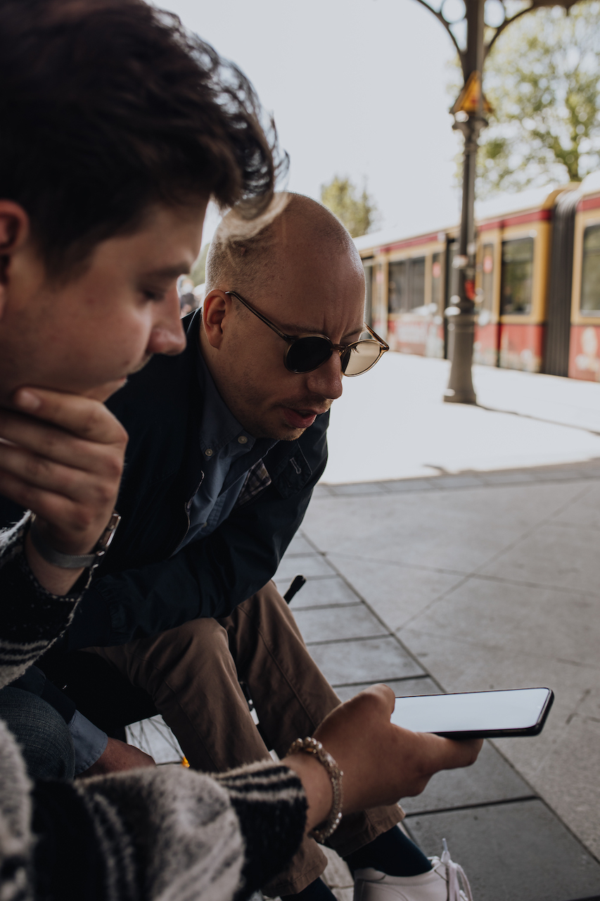 Zwei Männer an einem S-Bahnhof schauen auf ein Smartphone